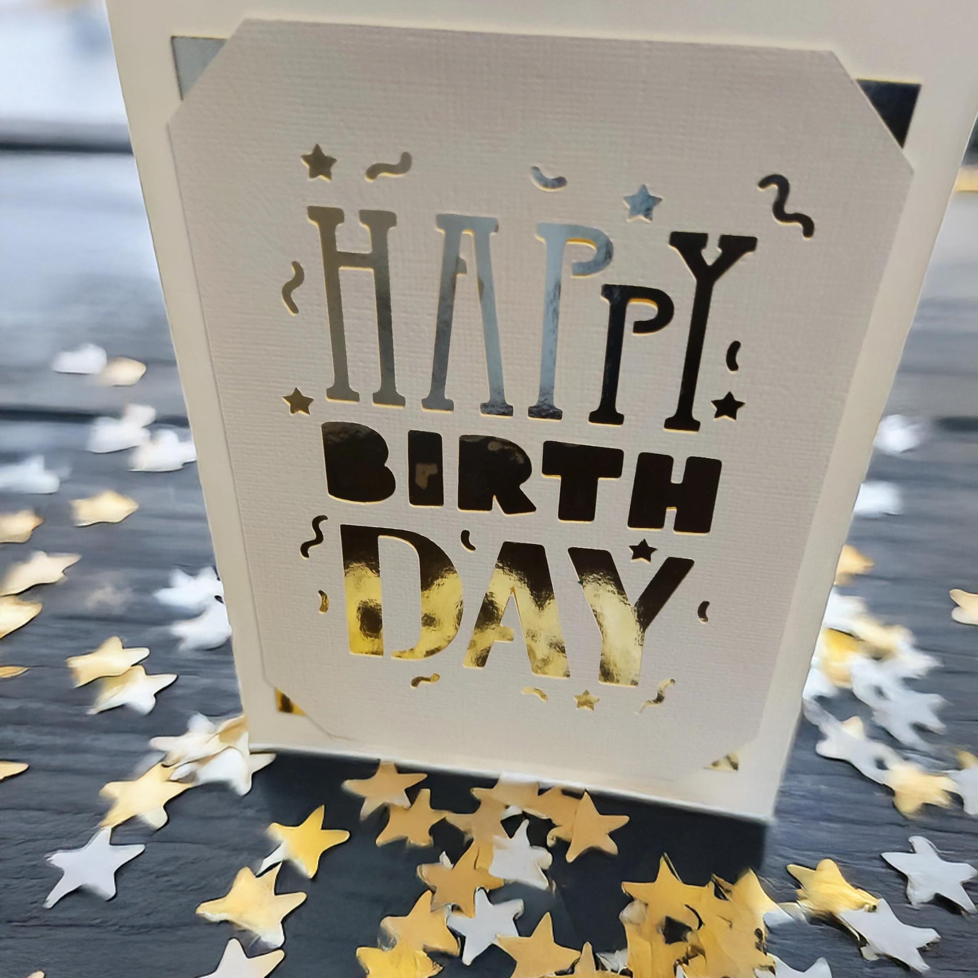 Close-up of a white laser-cut "Happy Birthday" card holder with star confetti.