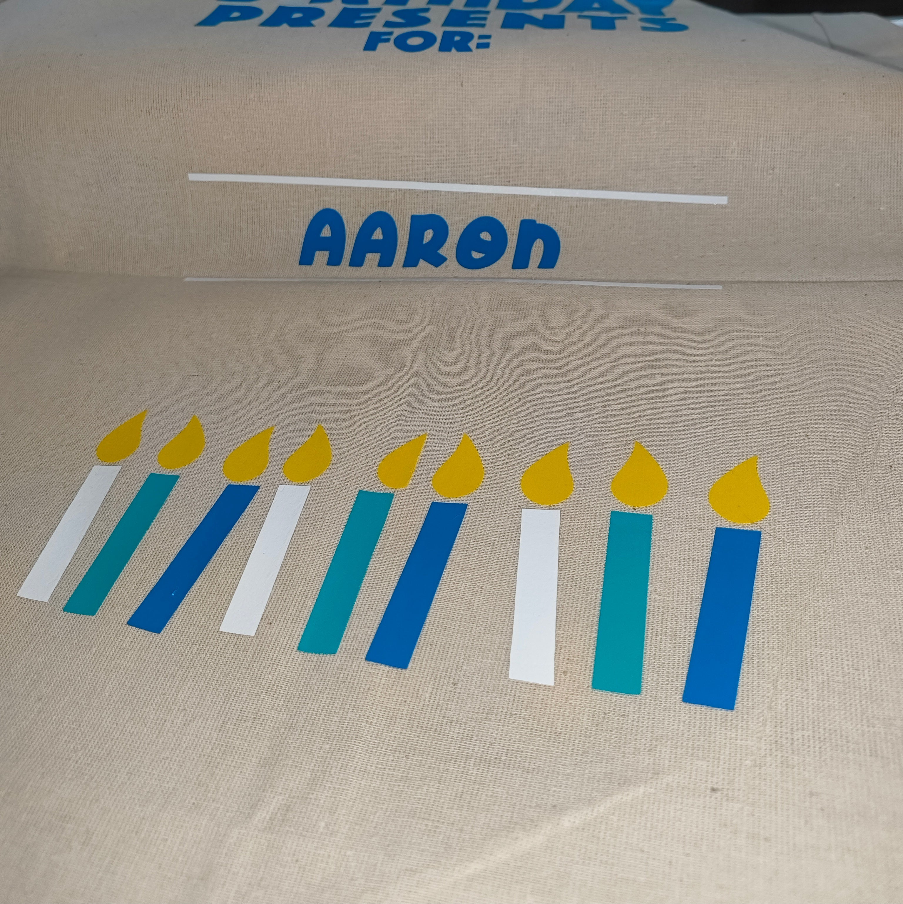 Personalised birthday gift bag with blue and teal candles and yellow flames, name Aaron in blue vinyl on natural cotton sack

