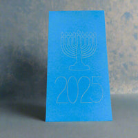 A bright blue Hanukkah card featuring a minimalist white outline of a menorah with nine candles above the year '2025'. The card stands upright against a softly textured grey and blue background, evoking a festive and elegant atmosphere.