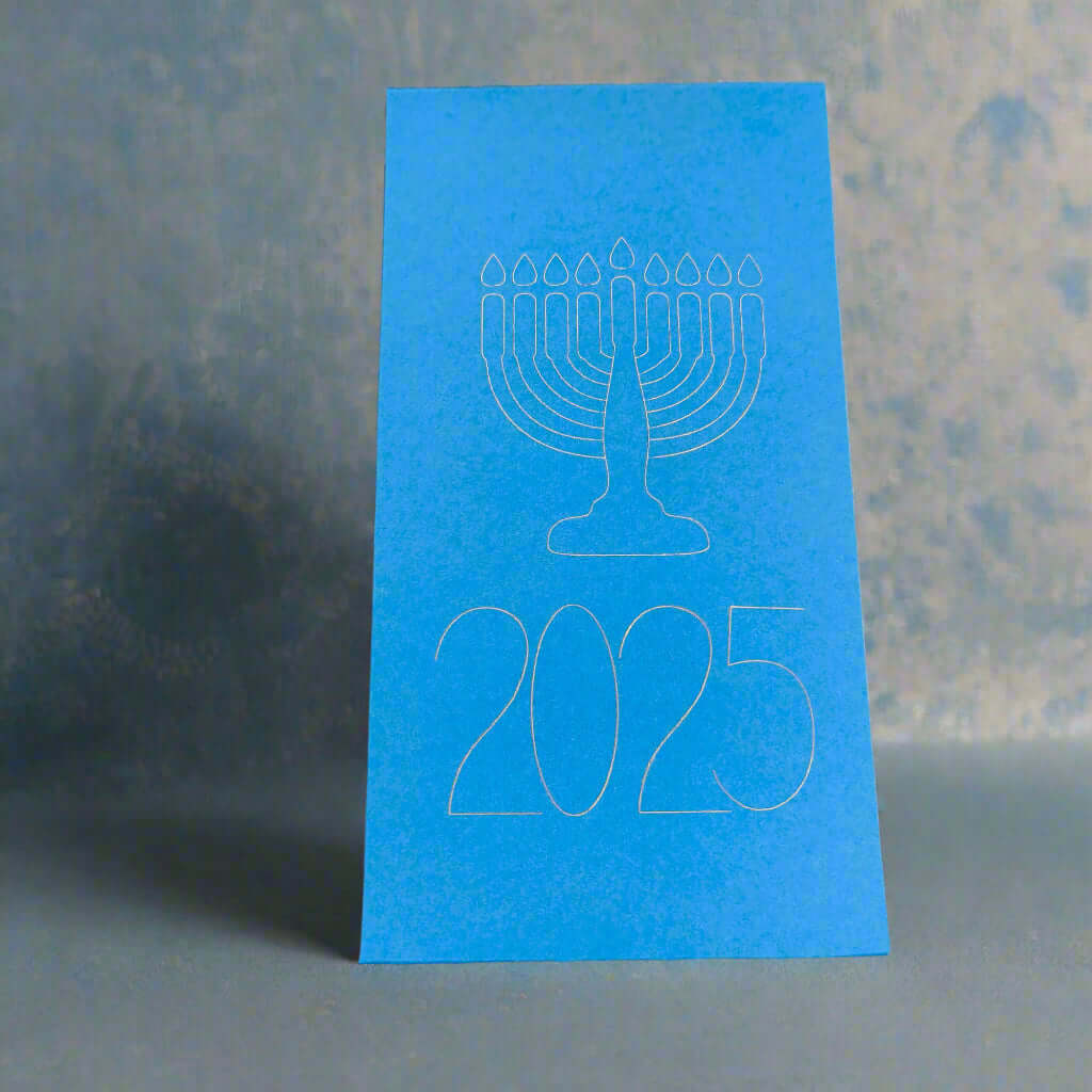 A bright blue Hanukkah card featuring a minimalist white outline of a menorah with nine candles above the year '2025'. The card stands upright against a softly textured grey and blue background, evoking a festive and elegant atmosphere.