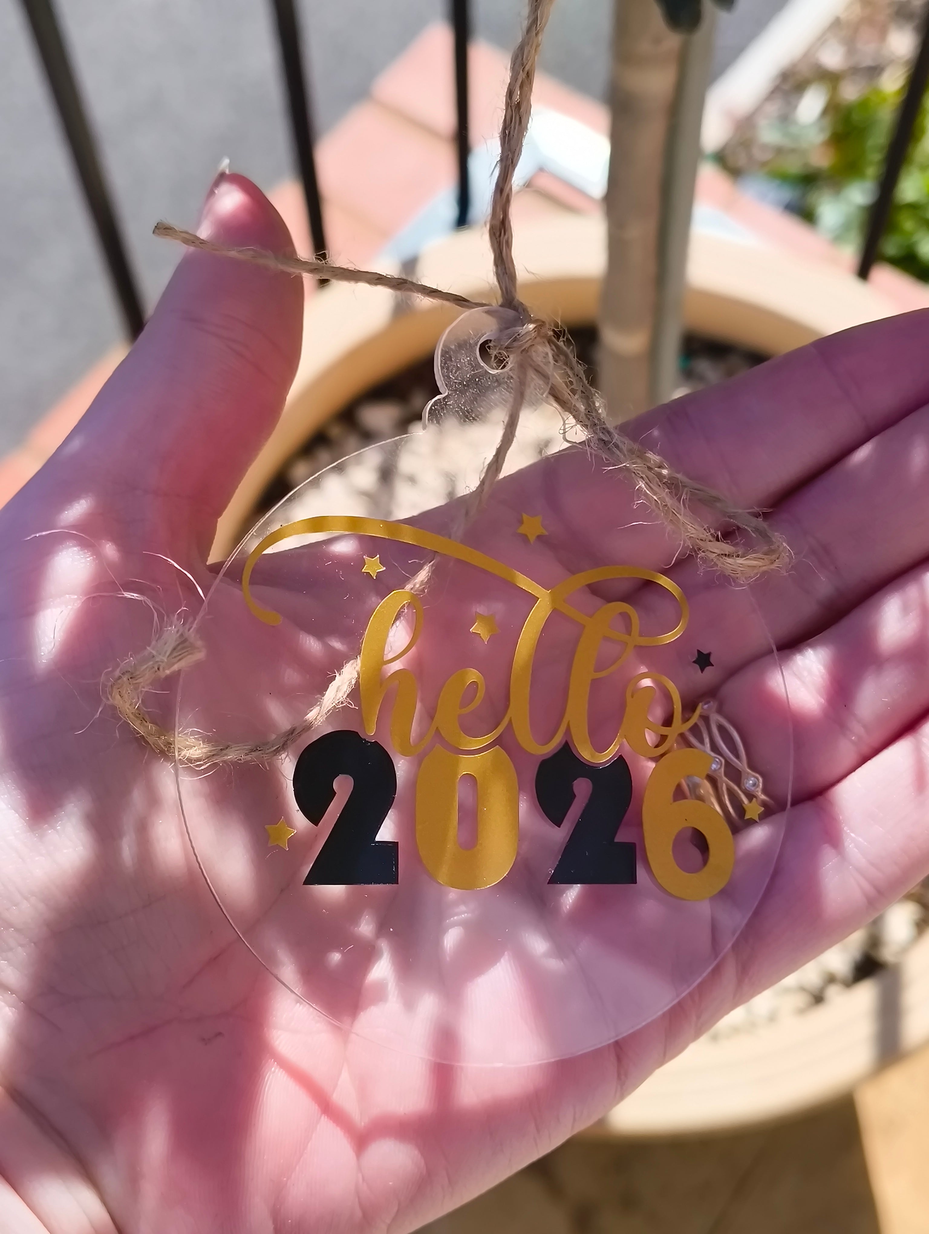 Hand holding a 2026 acrylic ornament with 'Hello 2026' design, perfect for New Year celebrations.