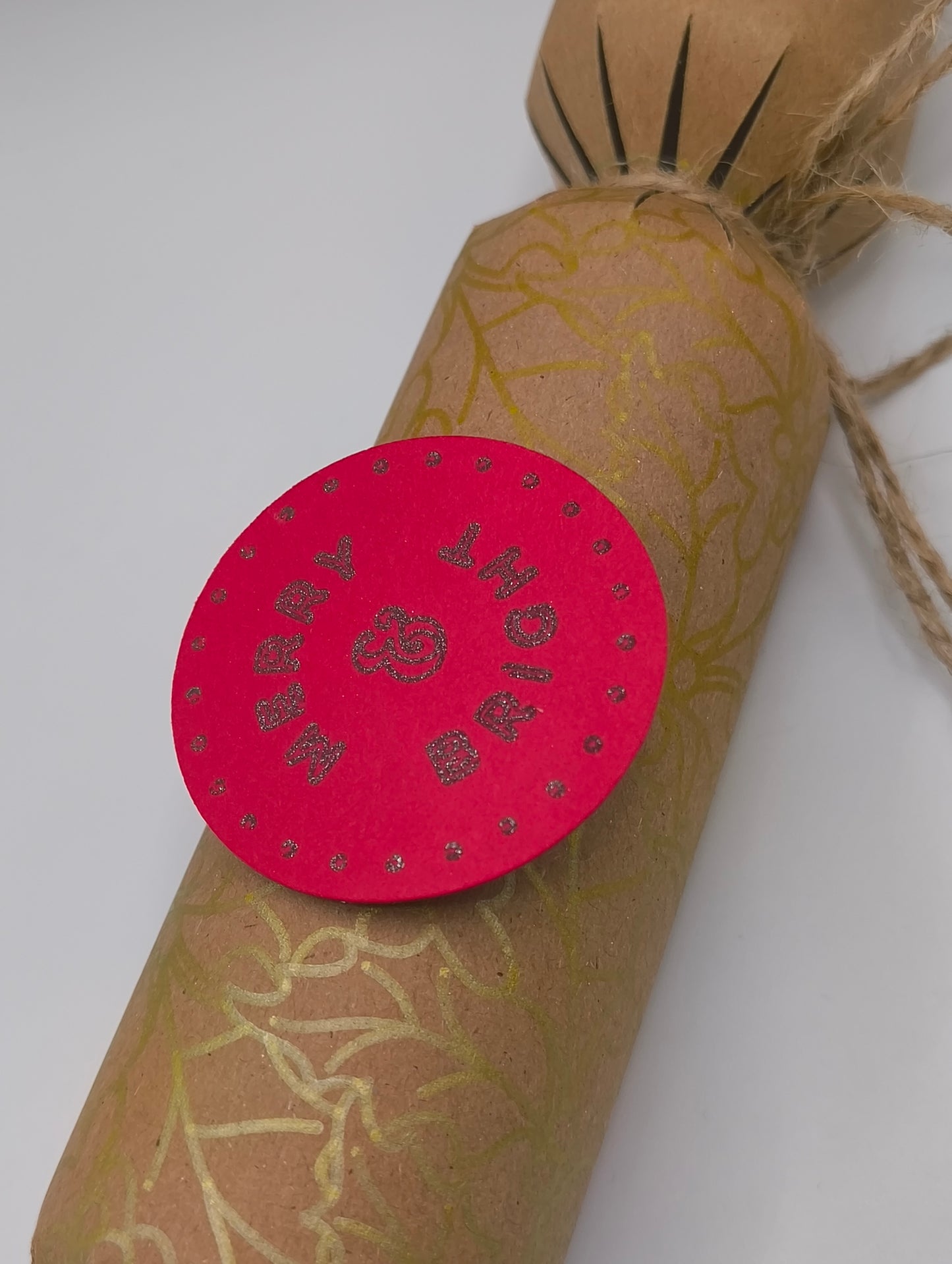 Eco-friendly Christmas crackers with gold holly design and festive pink tag, perfect for the holiday table.