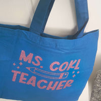 Personalised blue tote bag for teachers featuring glitter vinyl text that reads 'Ms. Gohl Teacher.' Perfect gift for educators.