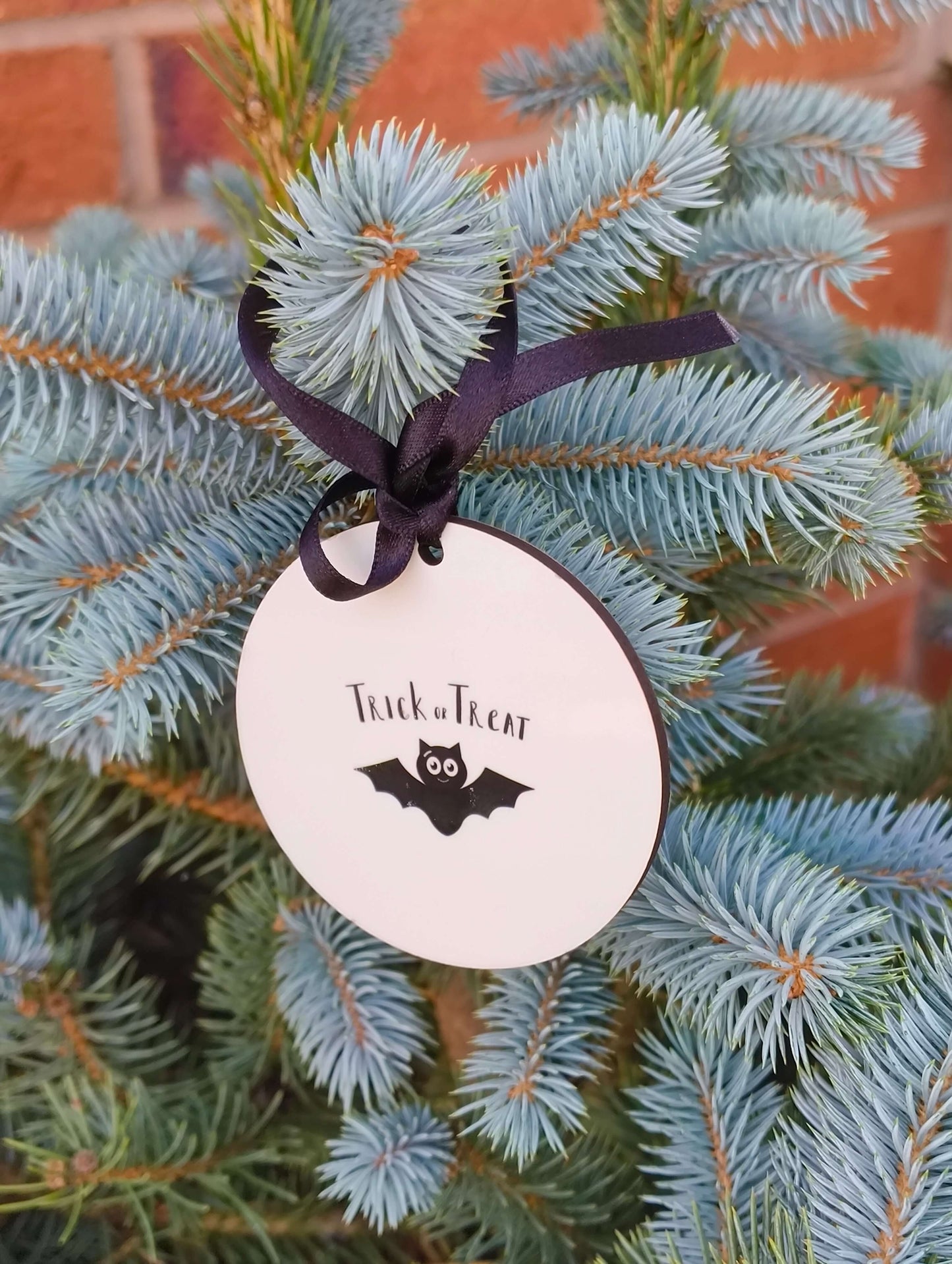 Trick or Treat Halloween bauble with bat design hanging on a pine tree adorned with black ribbon.