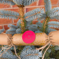 Eco-friendly Christmas crackers with gold holly design on a festive tree, showcasing rustic charm.