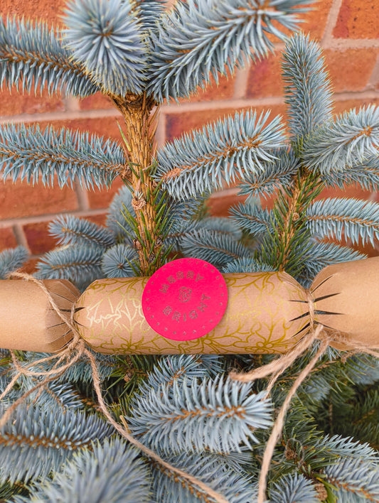 Eco-friendly Christmas crackers with gold holly design on a festive tree, showcasing rustic charm.