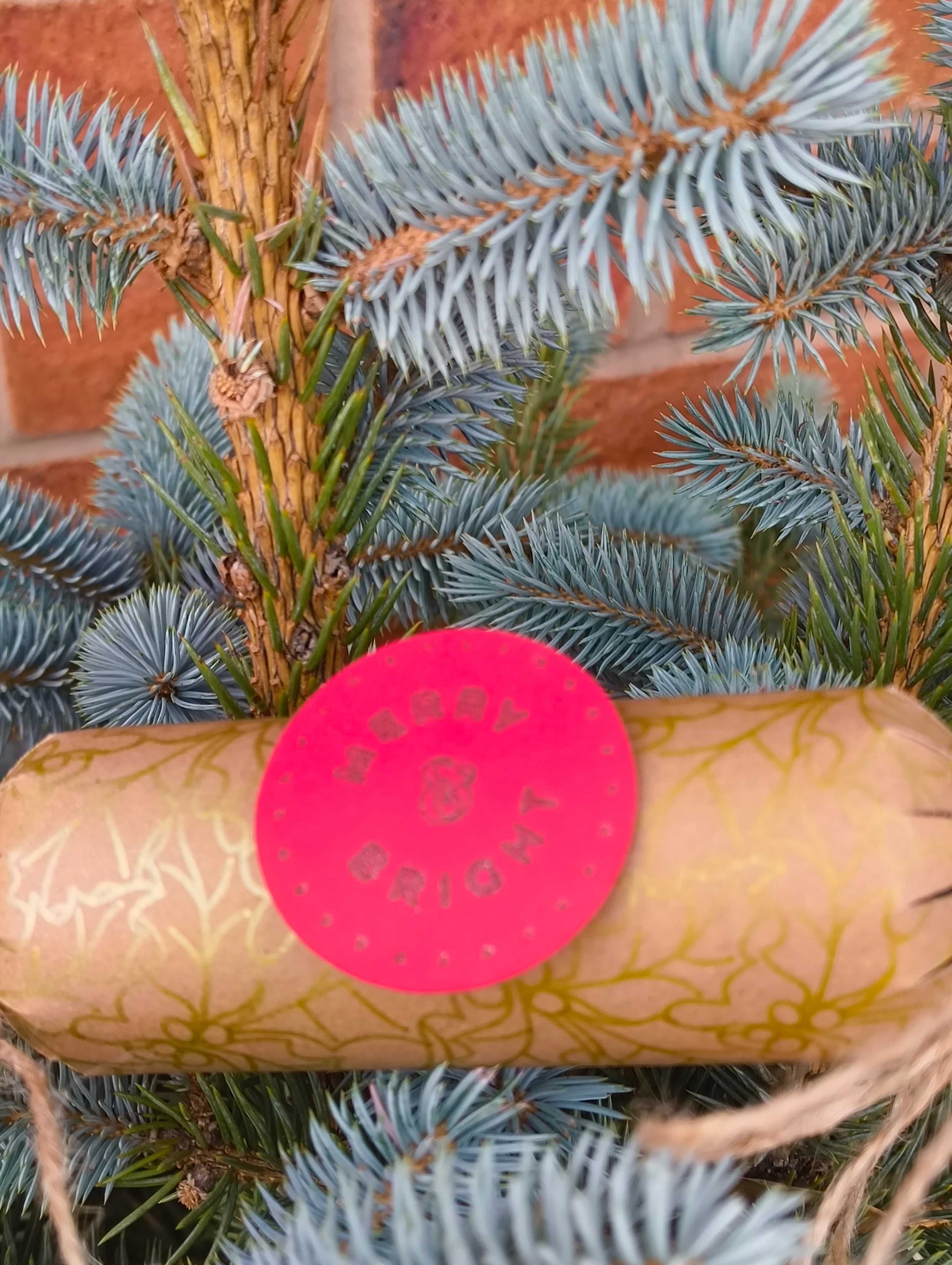 Eco-Friendly Christmas Crackers with gold holly design and jute twine on a Christmas tree.