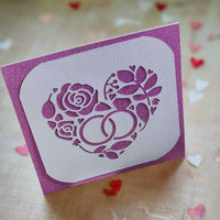 Handmade anniversary or wedding card with a sparkly purple background and a white die-cut intricate heart design with intertwined rings and roses.


