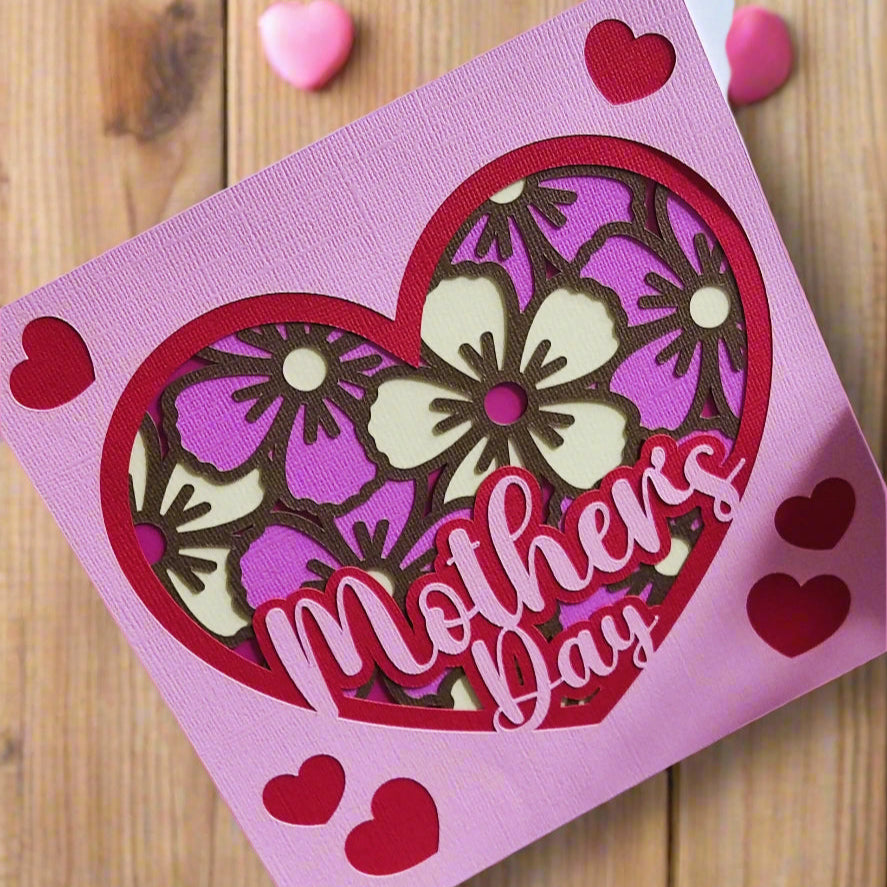 Handmade Mother's Day floral heart card in pink and purple with floral design and cut-out letters on wooden background.