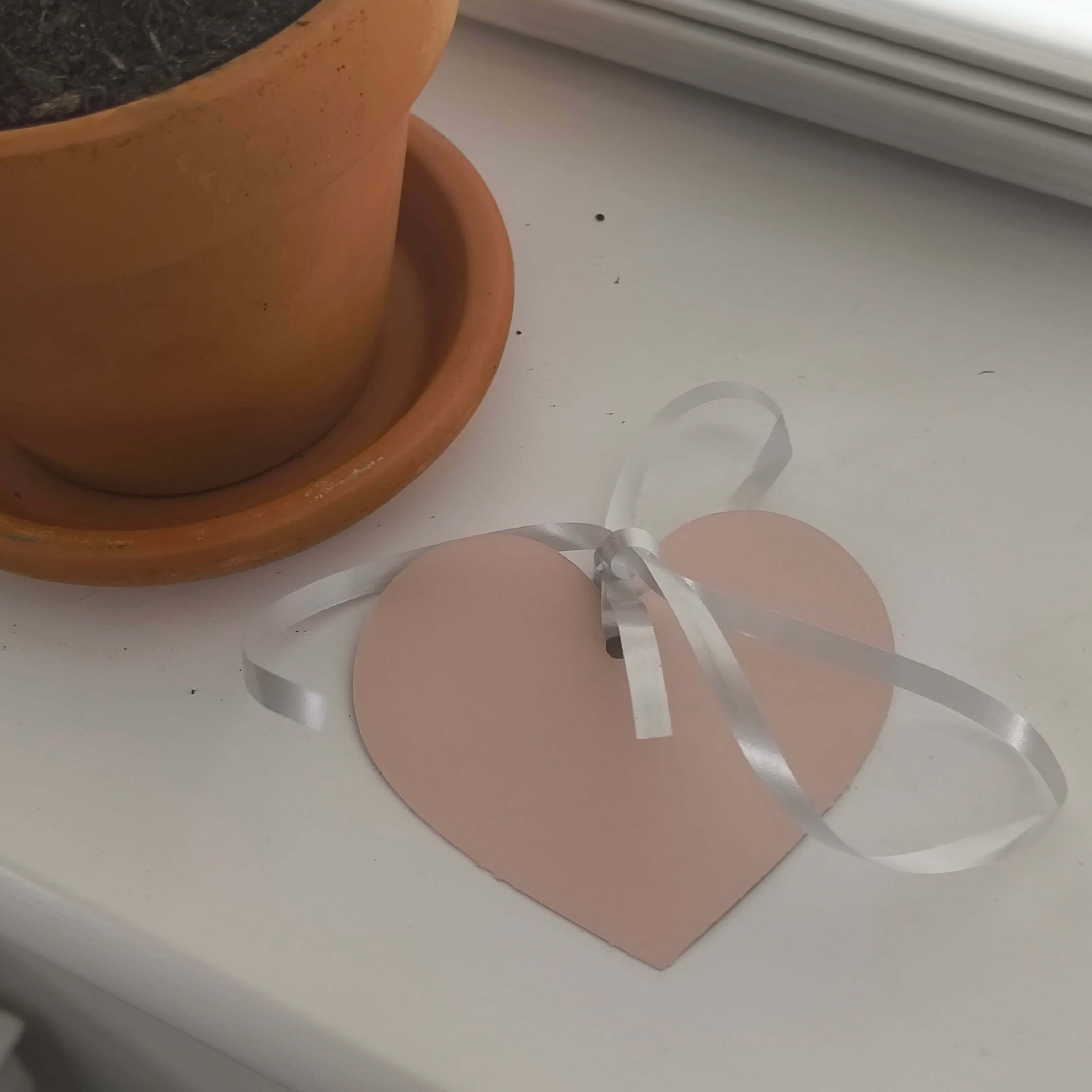 Personalised heart-shaped baby gift tag with silver ribbon next to a terracotta pot.