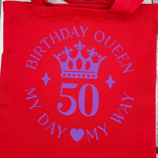 Red birthday queen tote bag laid flat, purple crown design with number 50.