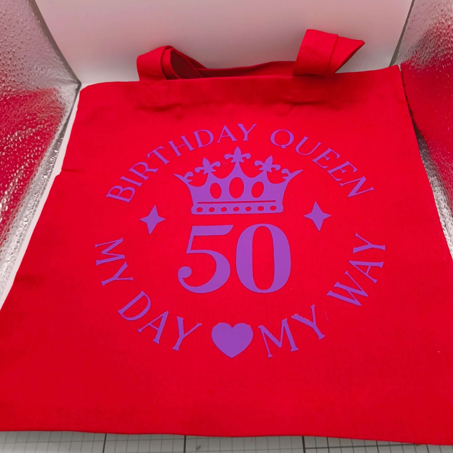 Red tote bag with purple crown and "Birthday Queen 50 My Day My Way" design displayed flat.