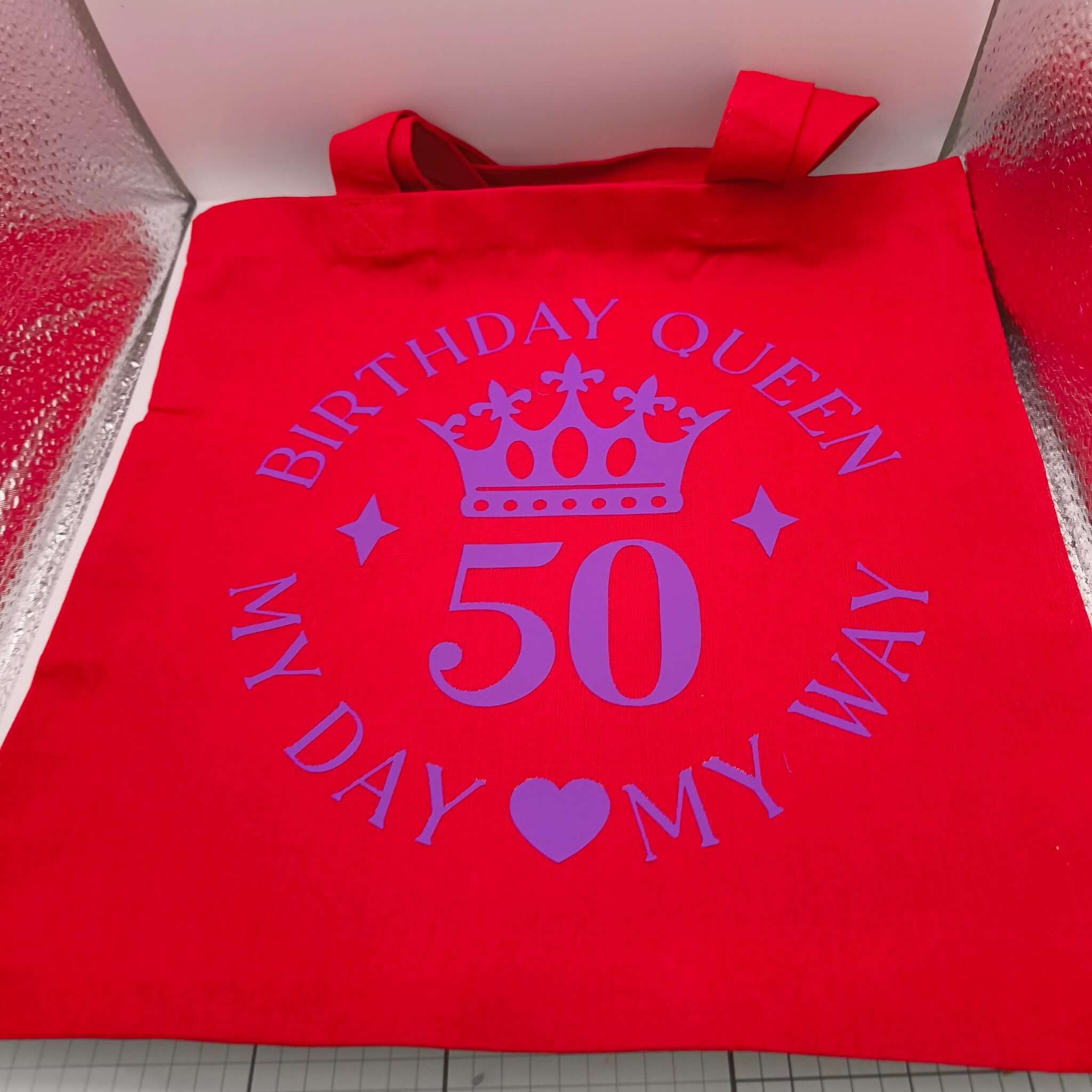Red tote bag with purple crown and "Birthday Queen 50 My Day My Way" design displayed flat.