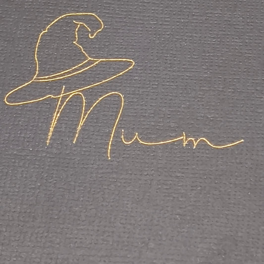 Extreme close-up of gold witch hat and “Mum” wording on black textured cracker card