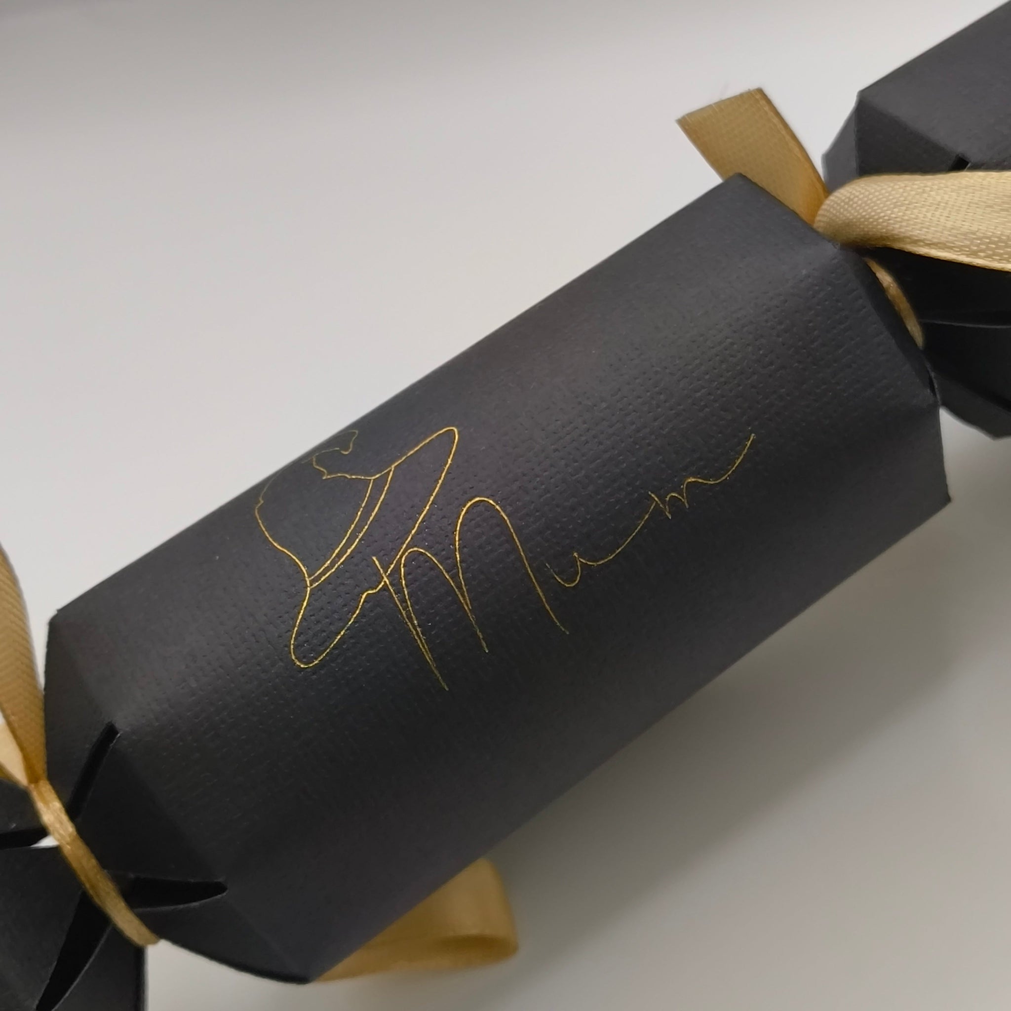Side view of assembled black cracker with gold foil witch hat “Mum” wording and ribbon ties