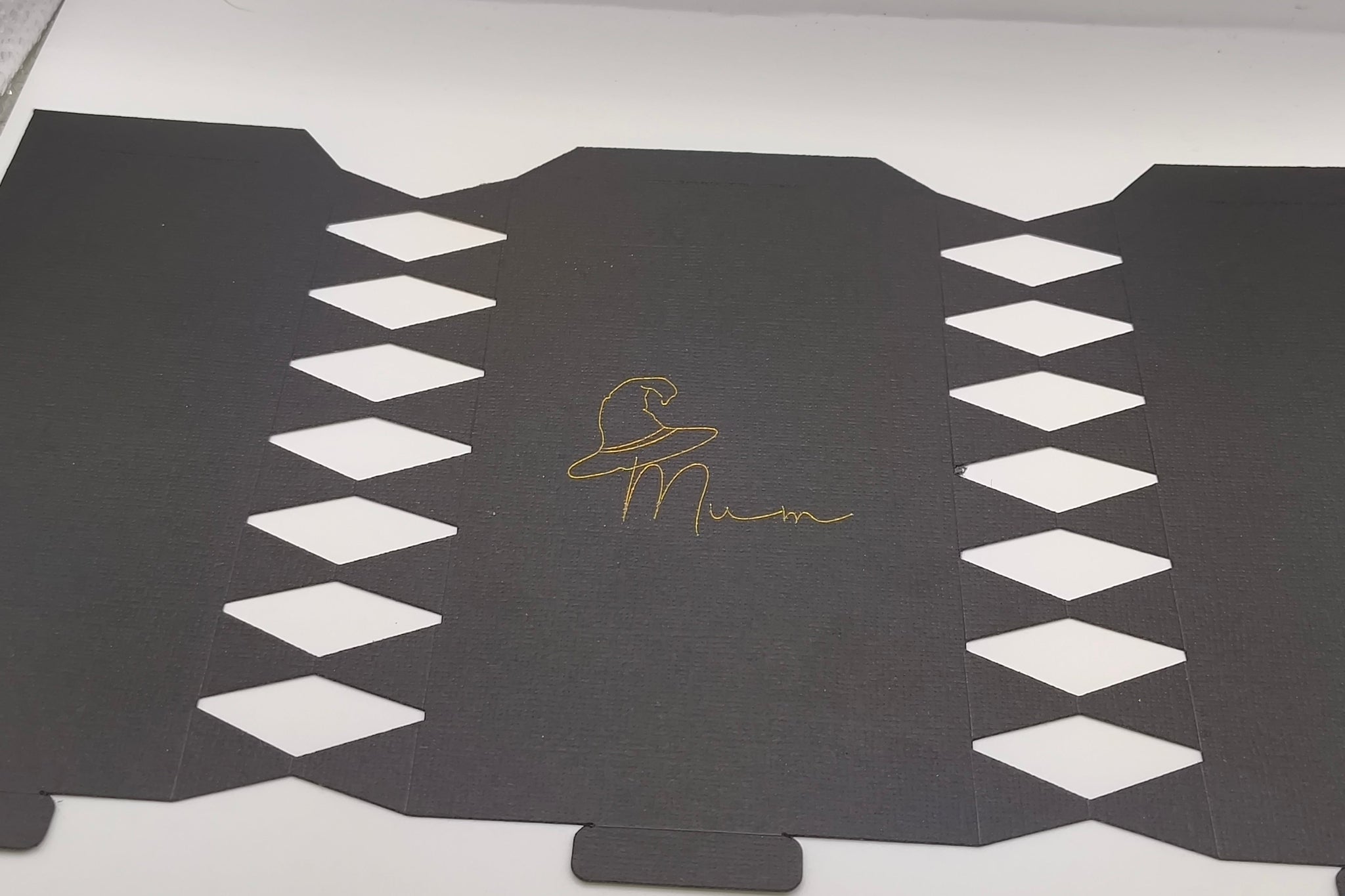 Flat black cracker template with diamond cut-out edges and gold foil witch hat “Mum” design in the centre