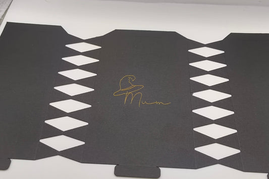 Flat black cracker template with diamond cut-out edges and gold foil witch hat “Mum” design in the centre