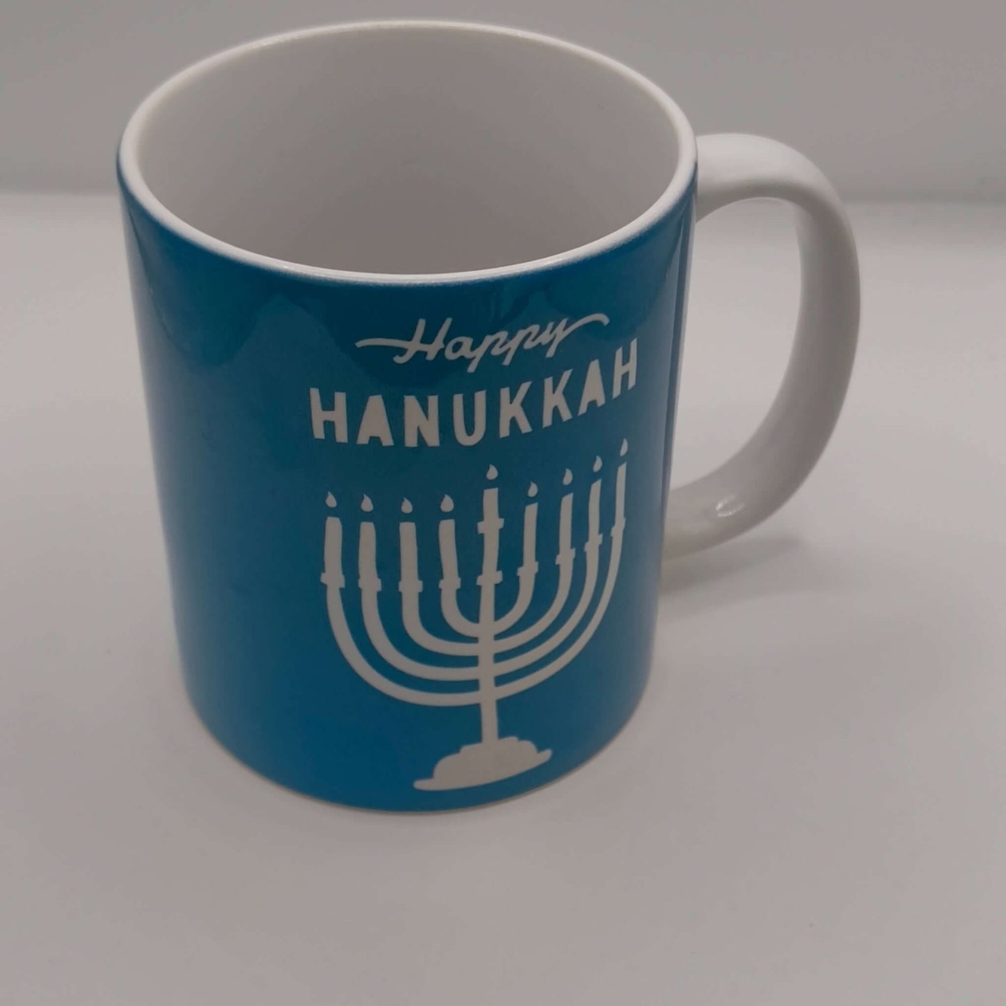 Happy Hanukkah mug with menorah design on blue ceramic coffee cup.