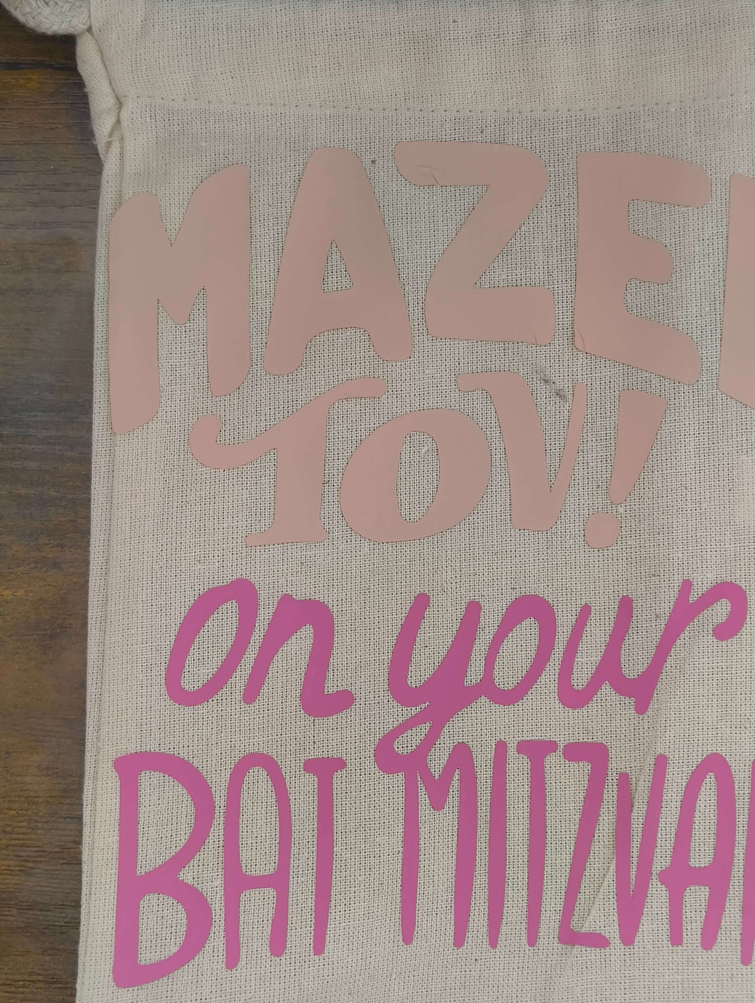Close-up of a personalized Bat Mitzvah gift bag with pink and blush lettering saying 'Mazel Tov! on your Bat Mitzvah'.
