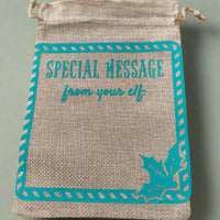 Burlap drawstring gift bag with turquoise vinyl text reading 'Special Message from your elf', framed with a candy cane-style border and a holly leaf design in the bottom right corner.