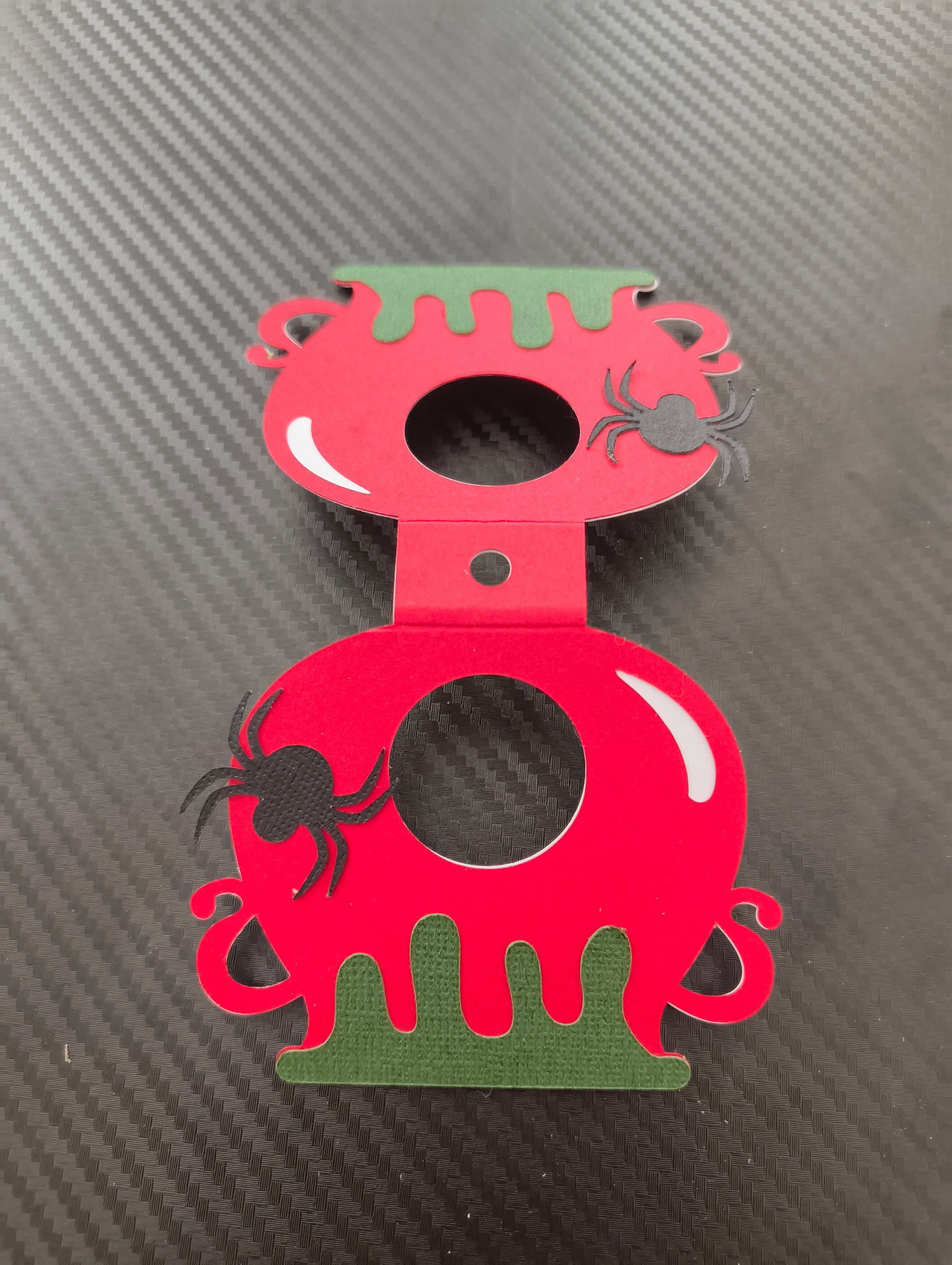 Red and green Halloween lollipop holder designed like a cauldron with spider embellishments.