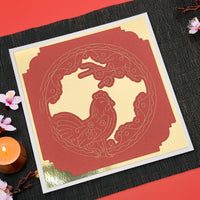Flat lay of a red and gold Chinese New Year rooster greeting card on a black placemat, handmade with layered cardstock, perfect for Lunar New Year celebrations.