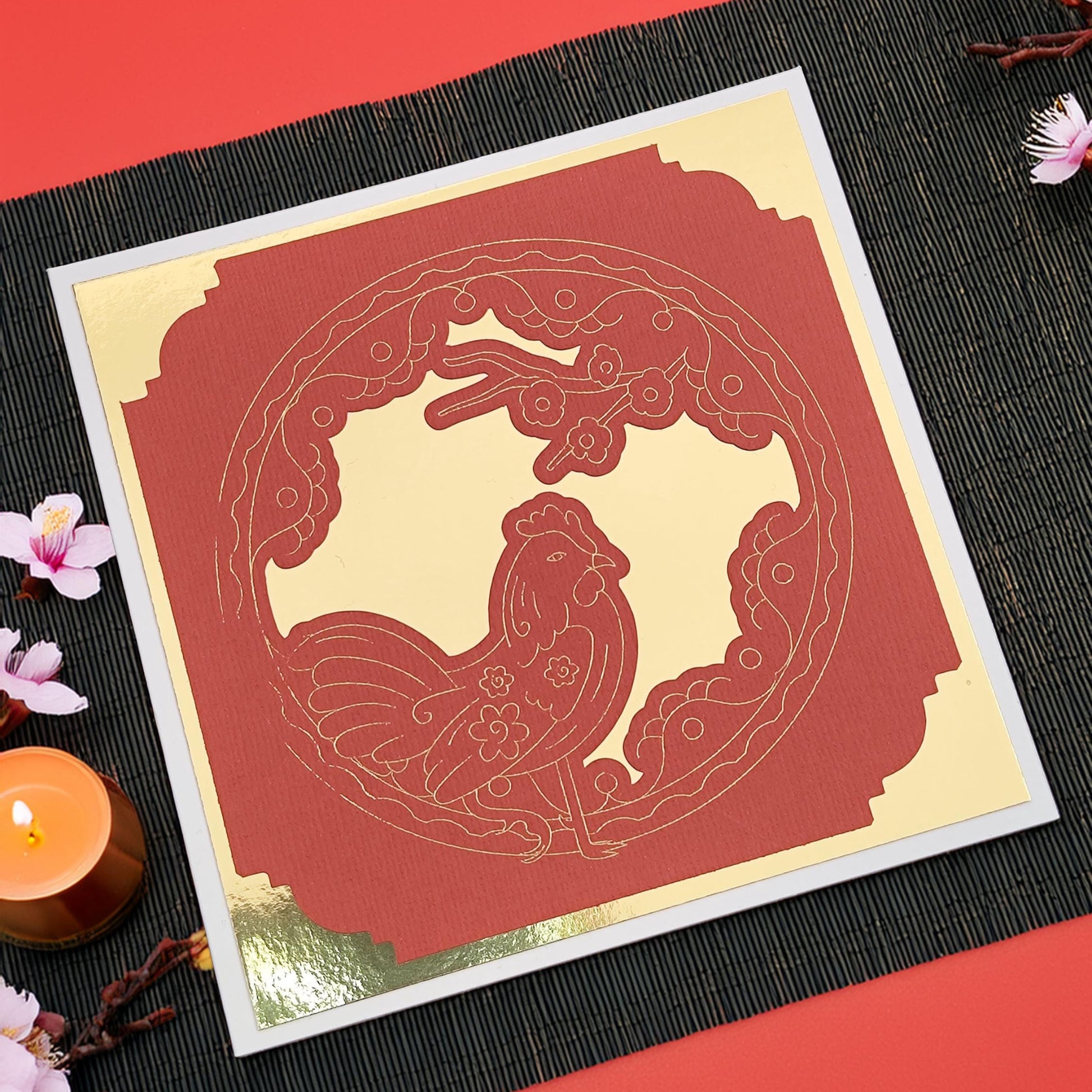 Flat lay of a red and gold Chinese New Year rooster greeting card on a black placemat, handmade with layered cardstock, perfect for Lunar New Year celebrations.
