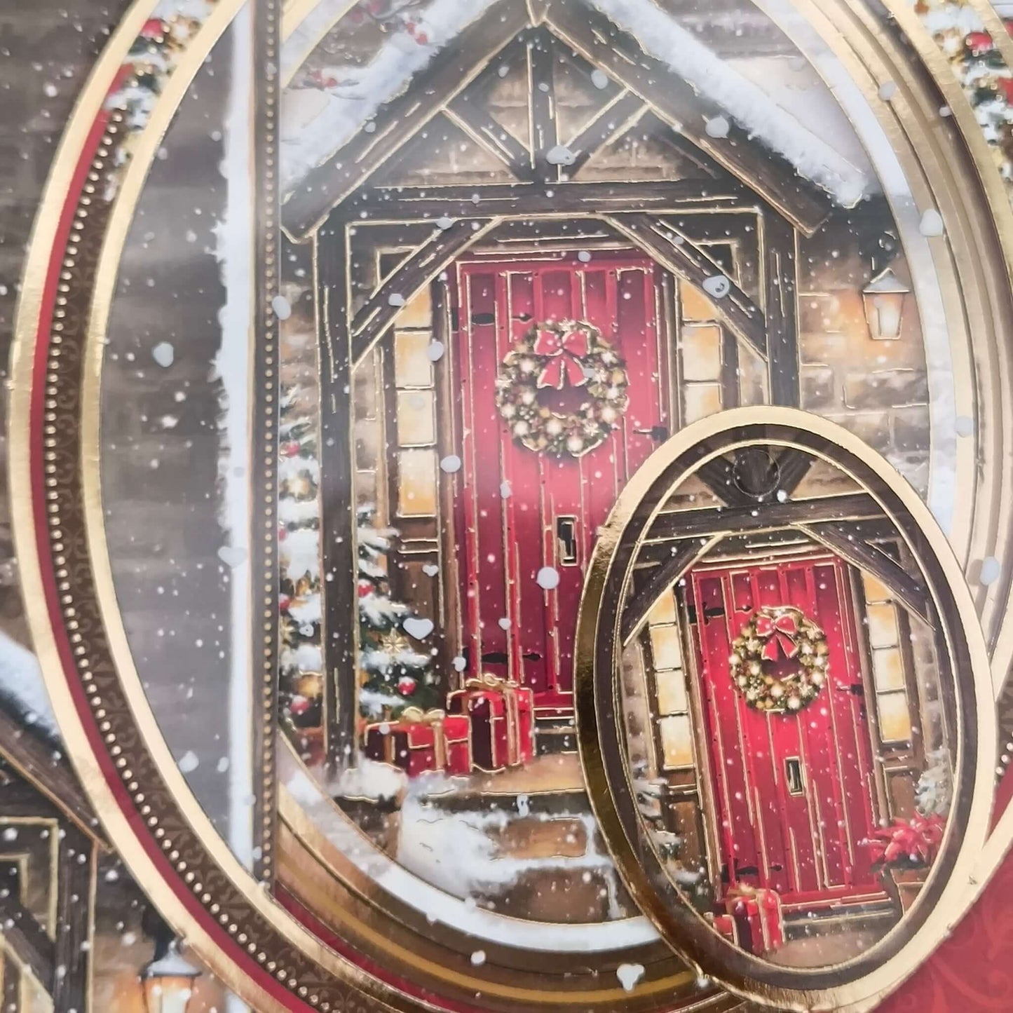 Layered oval topper close-up from handmade Christmas card showing snow, gold trim, and festive red front door.