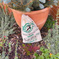 Canvas Christmas gift bag with green Reindeer Express print, customised with the name Stephen, photographed outside with festive greenery.