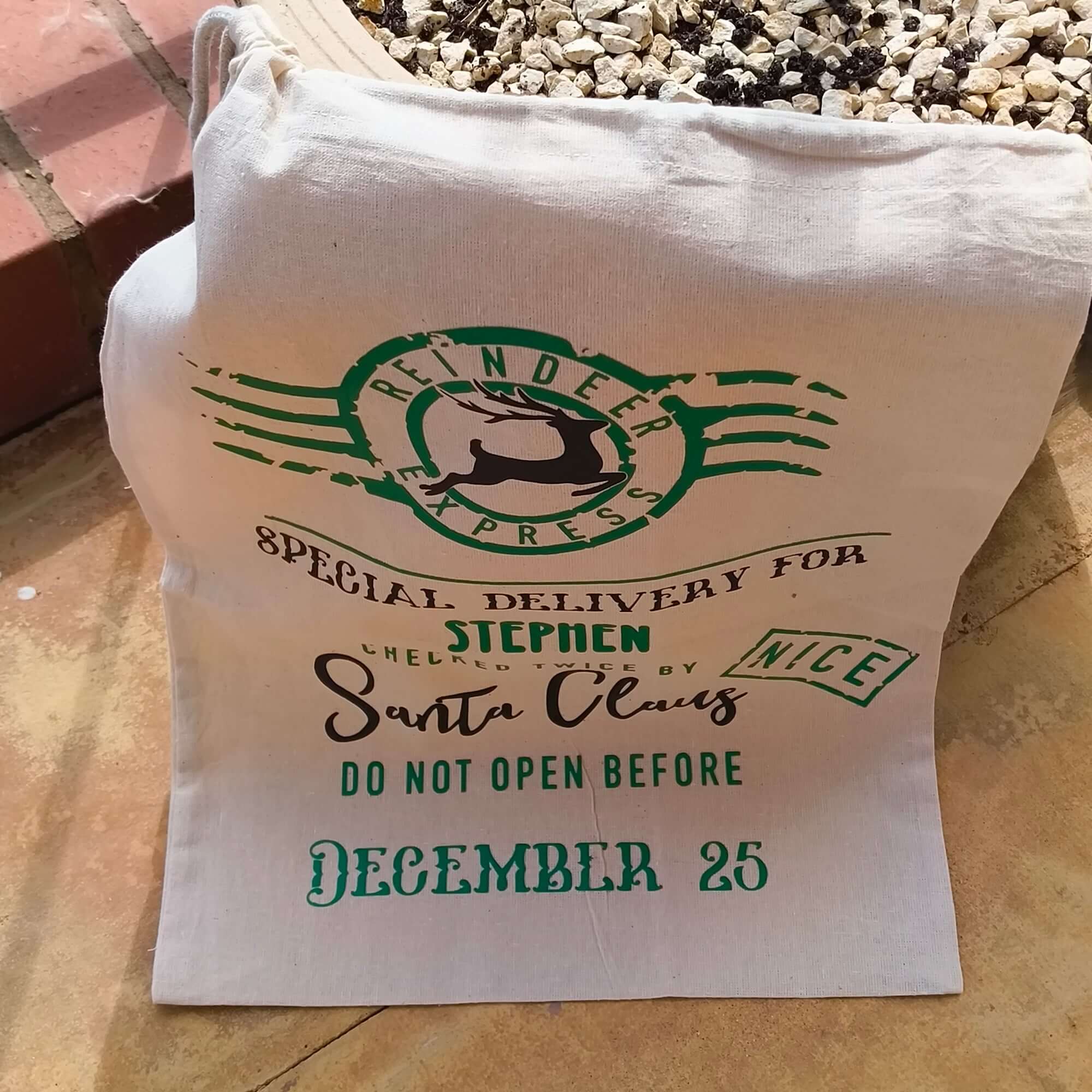 Close-up of personalised Christmas Santa sack with green and black festive typography, stamped “Nice” and marked with delivery from Santa Claus.