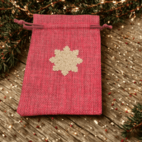 Gold snowflake gift bag in red hessian fabric on rustic wood, perfect for Christmas presents.