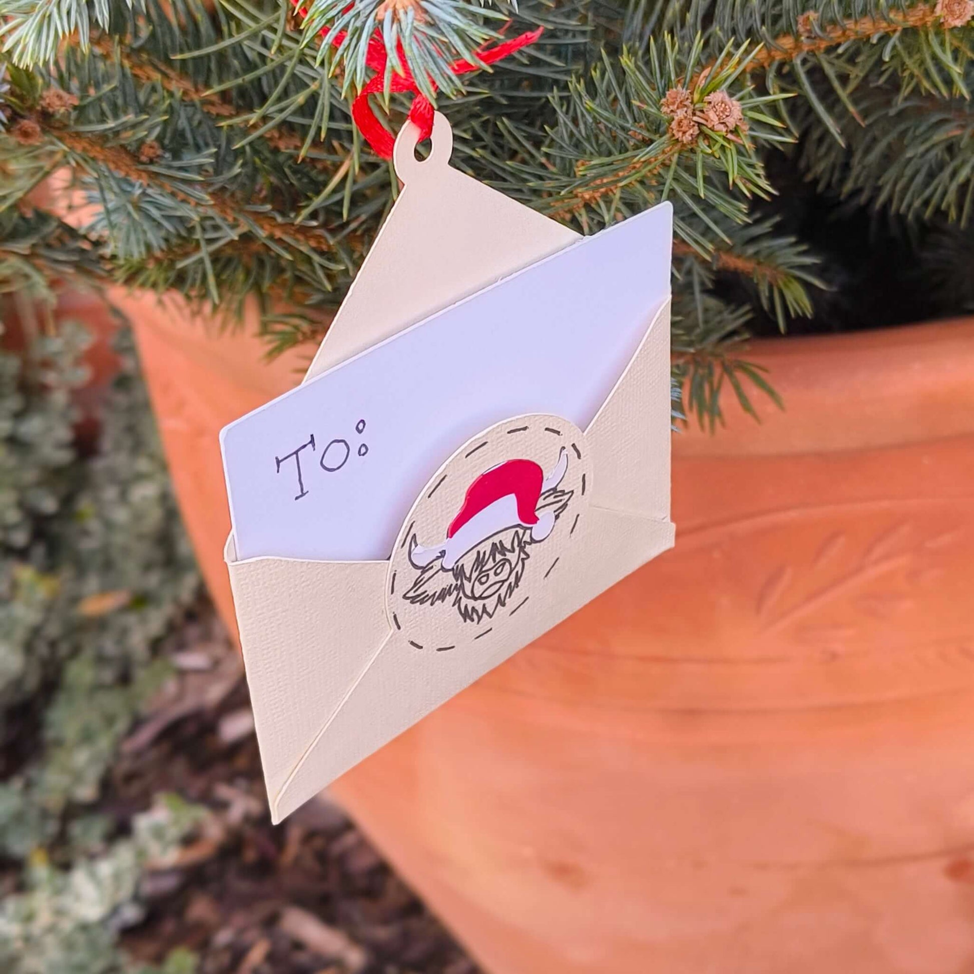 Handmade Christmas money holder ornament shaped like an envelope with Santa cow design hanging on Christmas tree branch