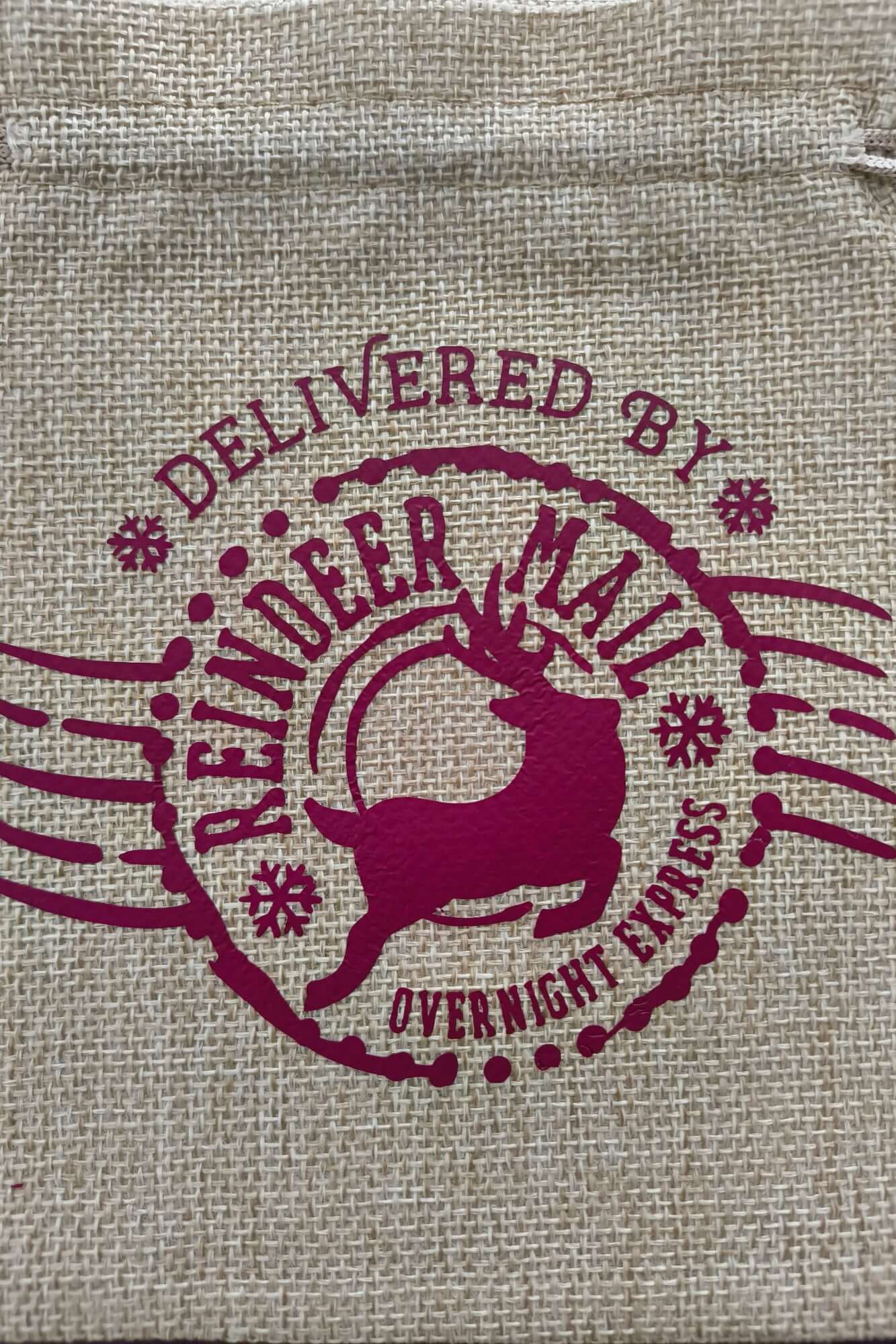 Close-up of reindeer and "Delivered by Reindeer Mail Overnight Express" text in burgundy print on natural hessian bag.