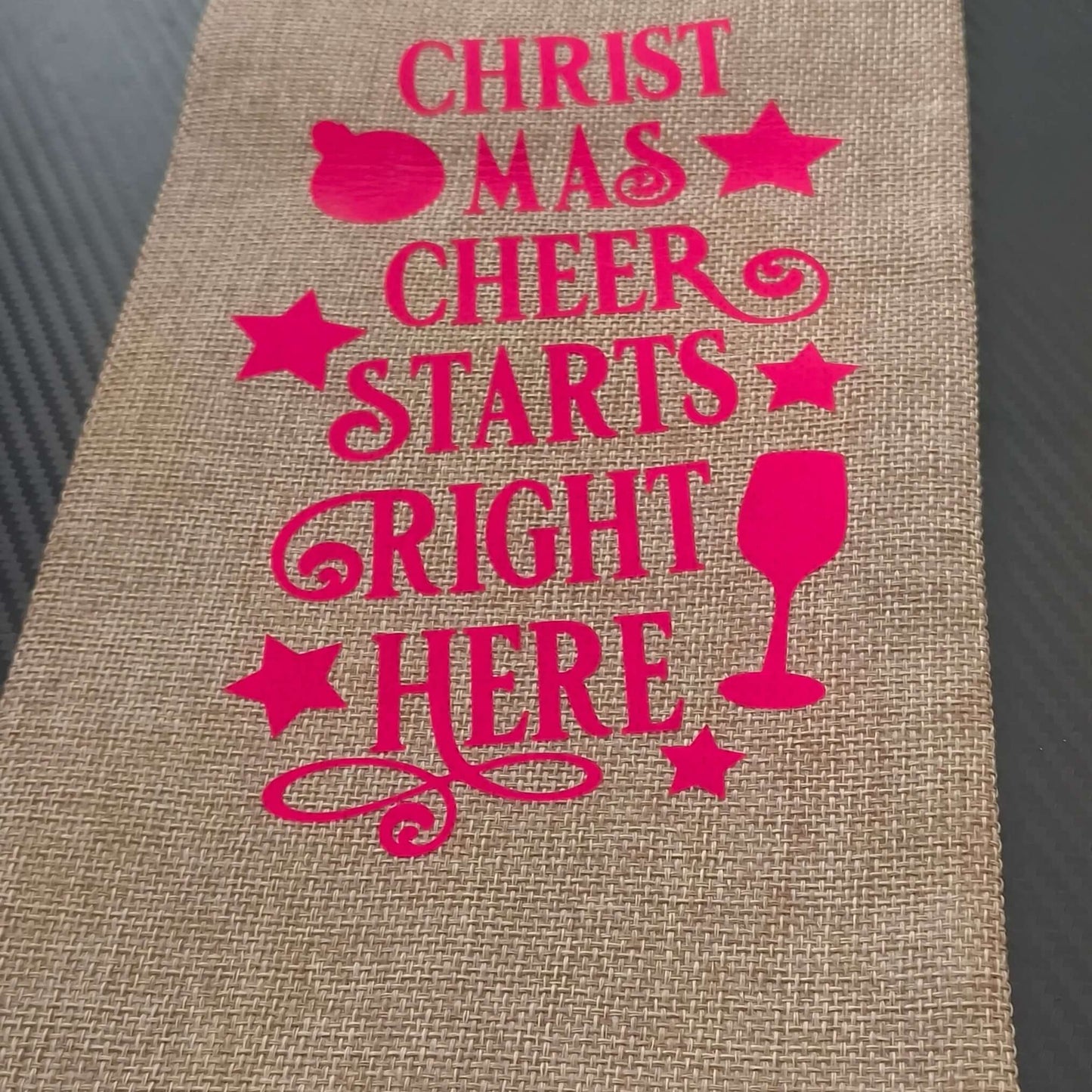 Festive hessian wine bag with pink lettering saying 'Christmas Cheer Starts Right Here', perfect for holiday gifting.