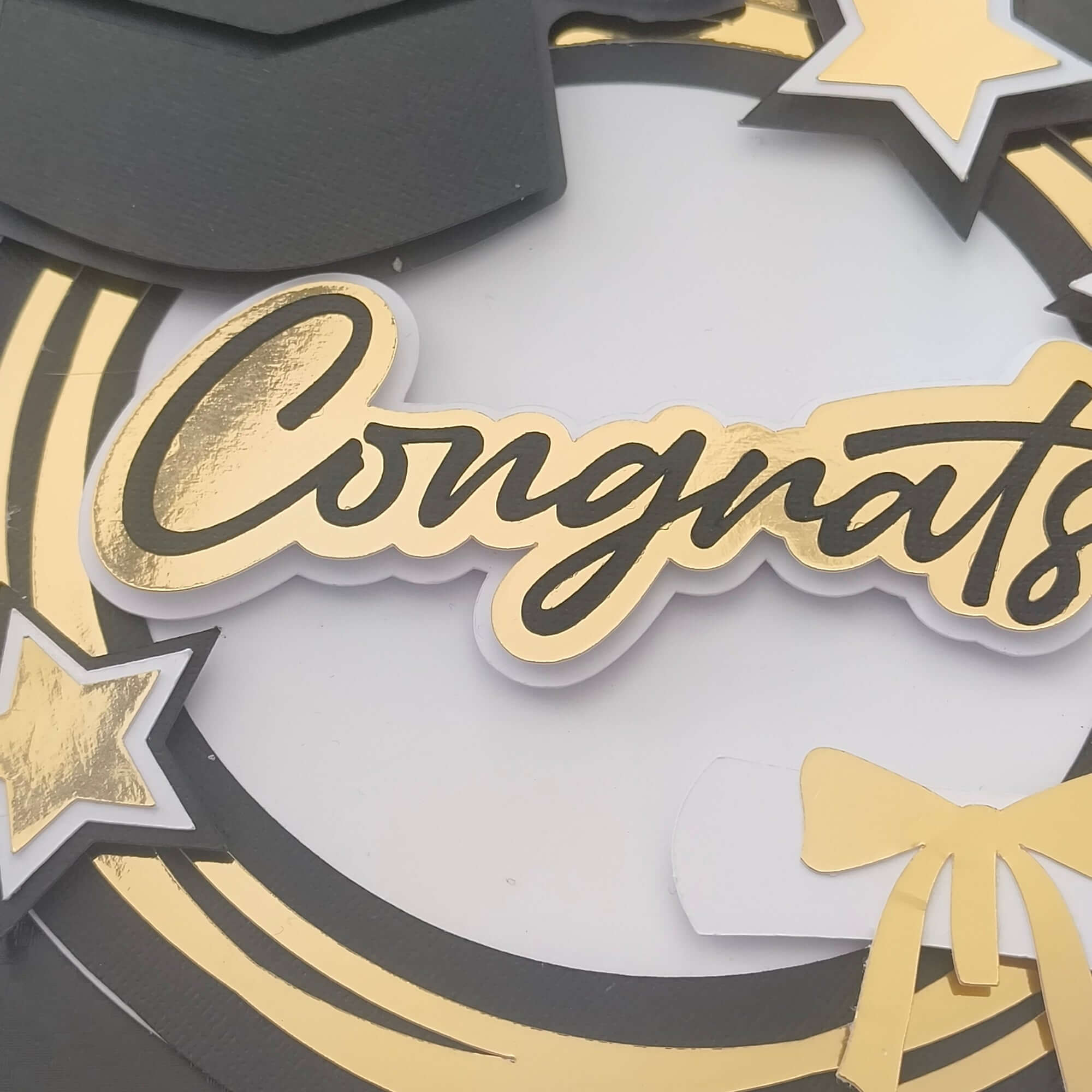 Close-up of handmade graduation card with gold foil “Congrats” text, black mortarboard, layered gold stars, and a diploma with yellow ribbon. Ideal for graduation cards and scrapbook embellishments.