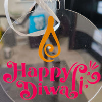 Close-up of clear acrylic Happy Diwali bauble with pink text and orange diya flame design, ideal for Hindu festive decor and gifts.