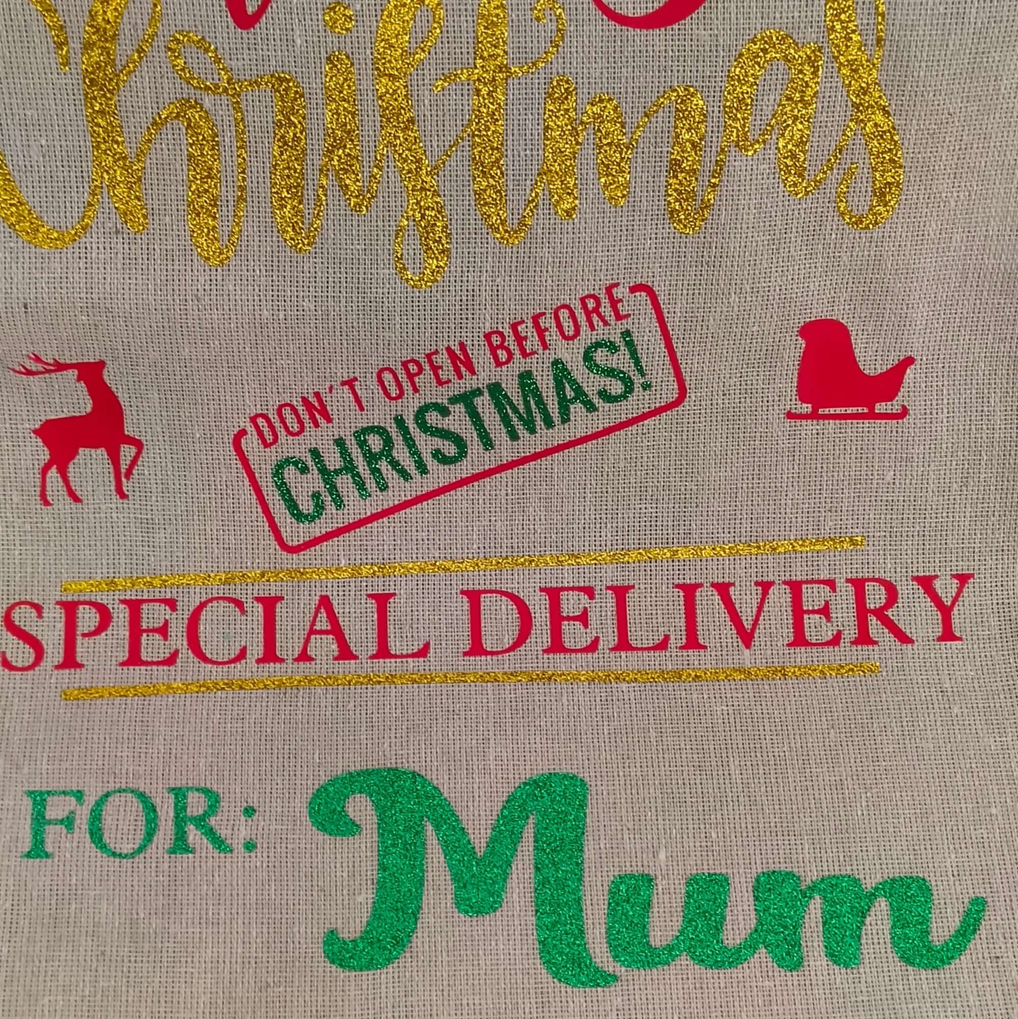 Close-up of personalised Christmas gift sack for Mum – gold glitter “Christmas” lettering, red sleigh and reindeer icons, green vinyl name detail, and festive “Don’t Open Before Christmas” stamp.