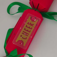 Close-up of red Christmas cracker showing gold ‘CHEER’ tag tied with green ribbon.