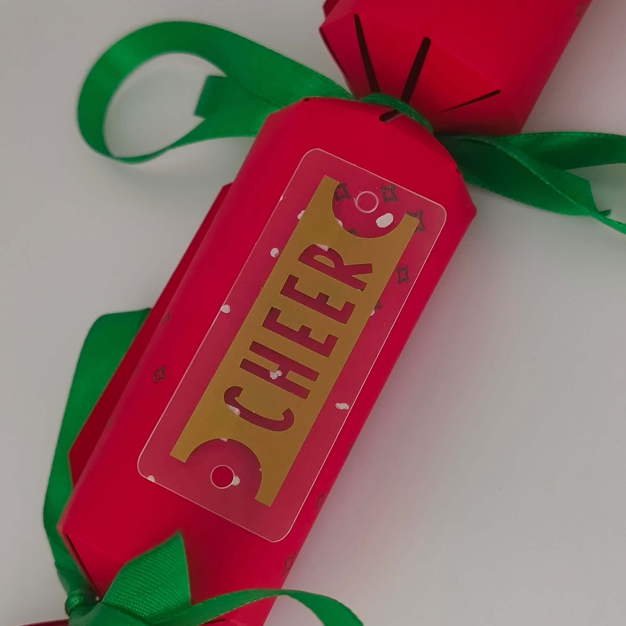 Close-up of red Christmas cracker showing gold ‘CHEER’ tag tied with green ribbon.
