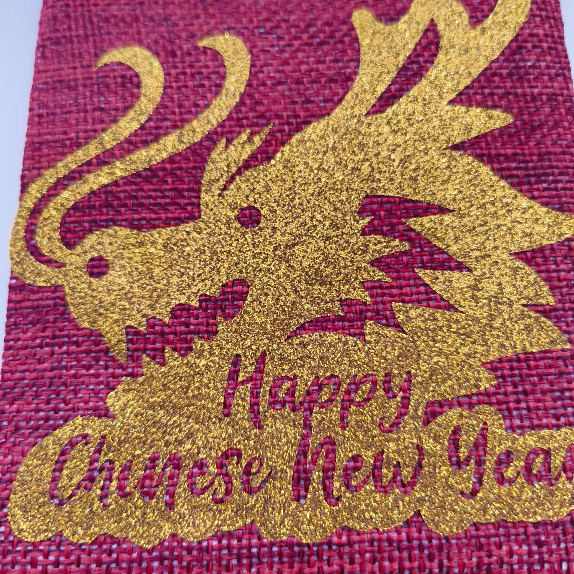 Close-up of glitter gold dragon design with “Happy Chinese New Year” text on red hessian bag.