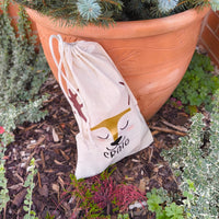 Natural cotton drawstring bag with reindeer illustration and name Craig, styled in garden with terracotta pot and greenery