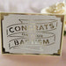 Handmade white and gold baptism card with cut-out lettering reading 'Congrats on Your Baptism', displayed on a soft pink surface with a white rose in the background.