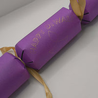 Handmade purple cracker close-up showing gold foiled “Happy Diwali” text with diya design in the centre.