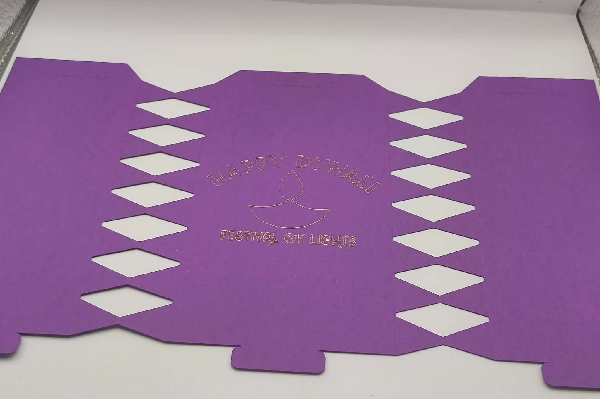Purple cracker design unfolded flat with cut-out diamonds and gold foiled “Happy Diwali Festival of Lights” message at centre.
