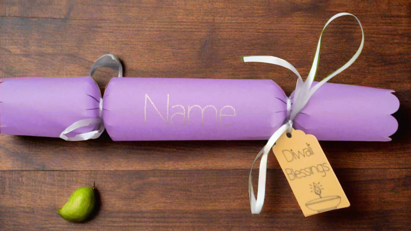 Personalised purple Diwali cracker with white ribbon and 'Diwali Blessings' gift tag, styled on a rustic wooden table with a green pear beside it.