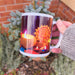 Hand holding a white Diwali-themed mug showing colourful diyas and a glowing mandala lantern design, photographed in a garden setting.