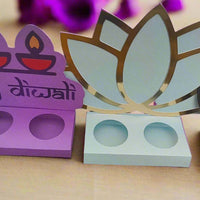 Front-facing image of a colourful set of three handcrafted Diwali sweet holders made from layered cardstock, featuring diya, lotus, and flame motifs on a warm-toned festive background.