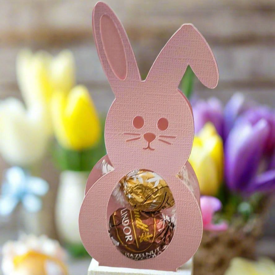 Pink Easter Bunny chocolate holder filled with Lindor truffles, displayed with yellow tulips in the background.