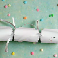 Handmade white Easter Bunny cracker with silver ribbon ties and cute vinyl bunny face on pastel background with colorful candy pieces scattered around.