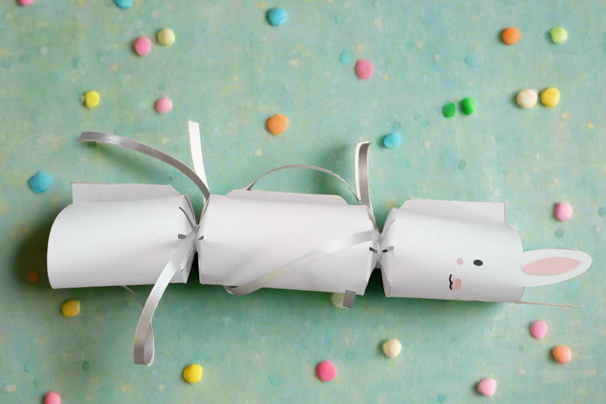 Handmade white Easter Bunny cracker with silver ribbon ties and cute vinyl bunny face on pastel background with colorful candy pieces scattered around.